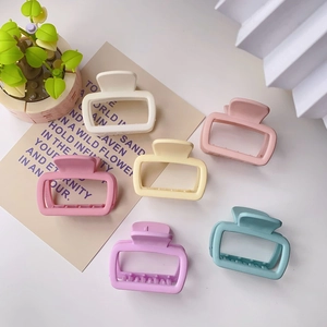 Flat lay of six matte square hair claws in soft pastel colors with decorative props