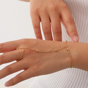 Detail of a minimalist gold slave bracelet with finger ring and dainty bead chain on hand