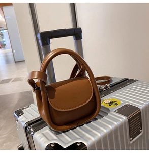 Détail d'un mini sac à main en cuir marron vintage posé sur une valise argentée