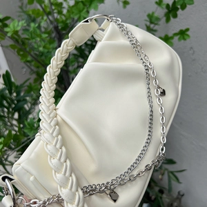 Detail of white PU cloud bag featuring woven handle and silver chain with heart charm