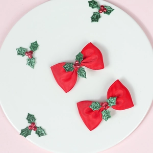 Close-up of red grosgrain bow hair clips with green holly leaves and red berry accents