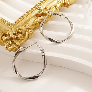 Minimalist C-shape twisted silver earrings displayed on a modern white stair stand