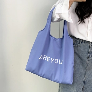 Detail of light blue canvas tote bag featuring white AREYOU lettering shown on model