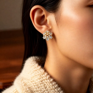 Detail of 14k gold plated snowflake earrings with zircons worn by a model in soft light