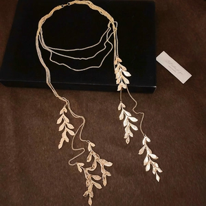 Detailed close-up of a multi-layer golden leaf pendant necklace on premium suede texture