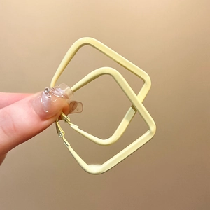 Close-up of a hand holding large square yellow metal hoops with smooth matte finish