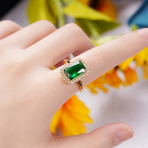 Macro detail of gold-plated ring featuring a large green emerald-cut stone and halo diamonds