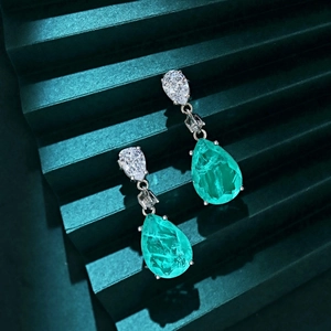 Macro detail of tear-drop emerald and cubic zirconia earrings in silver setting