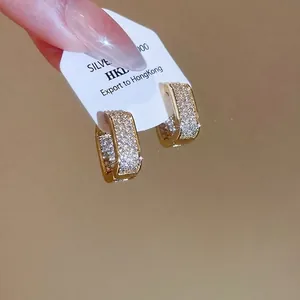Sparkling square zircon hoop earrings in warm gold finish held by hand on a warm background