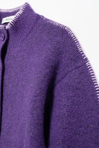 Dettaglio del cardigan in maglia viola con cuciture bianche e bottone sul collo