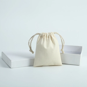 Close-up of minimalist cream cotton drawstring pouch next to a white jewelry display box