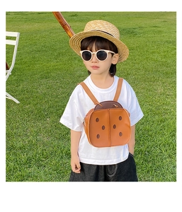 Toddler in a grassy field wearing a cute brown ladybug backpack with antenna details