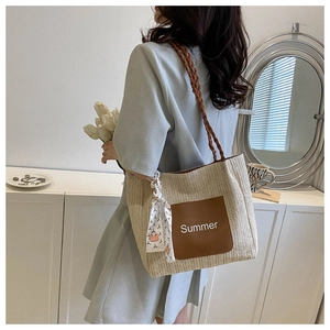 Détail du sac cabas en paille tressée avec poche en cuir marron et foulard en soie décoratif