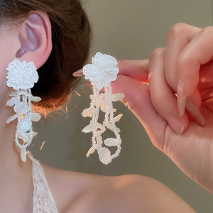 Detail of white floral stud earrings with cascading pearl tassels and leaf charms