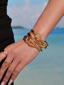 Detail of 18k gold plated stainless steel wave bangles and rings on female hand