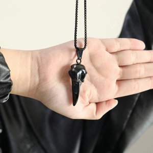 Detailed macro view of a black raven skull pendant on a necklace held by a hand