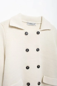 Détail du col à revers, des boutons croisés et de l'étiquette de taille sur le cardigan crème