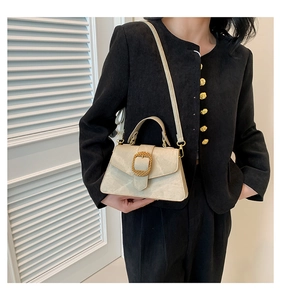 Detail of a beige matte leather handbag with a large gold buckle and slim shoulder strap