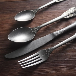 Vintage embossed stainless steel cutlery set with ornate handles on a wooden background
