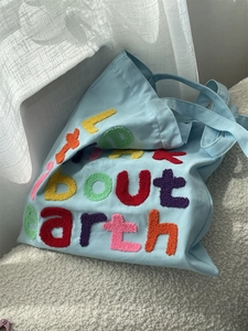 Detail of light blue canvas tote bag featuring colorful about earth towel embroidery texture