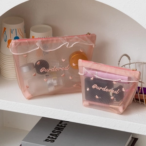 Pink mesh makeup bag set with heart embroidery and lace trim on a white shelf