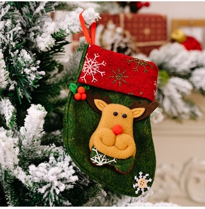 Close-up of a green Christmas stocking with reindeer applique hanging on a pine branch