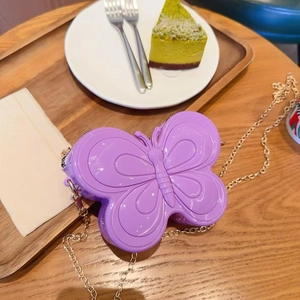 Détail d'un sac papillon violet en gelée avec une bandoulière chaîne dorée sur une table en bois