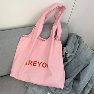 Pink canvas tote bag featuring red ARE YOU letter print on a cozy sofa setting