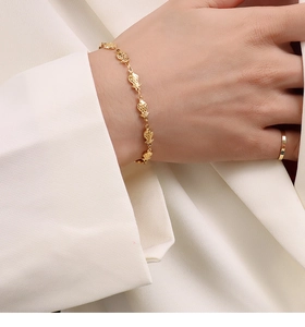 Close-up of golden fish-shaped bracelet links on wrist with a minimalist ring