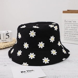 Close-up of black cotton bucket hat with white daisy print on a minimalist wooden table