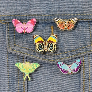 Colorful butterfly and moth enamel pins set displayed on a blue denim jacket pocket