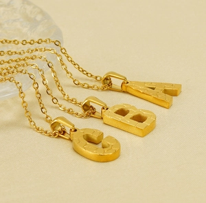 Detail of 18K gold stainless steel letter pendants with faceted crystal surface texture