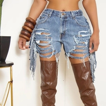 Detail shot of distressed denim shorts in blue featuring frayed edges and tassel hem
