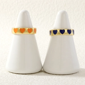 Detail of gold rings with orange and dark blue enamel heart charms on white stands