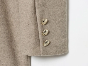 Detail of beige wool blend coat sleeve with three decorative gold embossed buttons