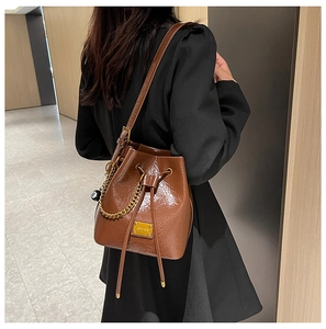 Sac seau marron brillant avec cordon de serrage, chaîne dorée et breloque boule 8 porté