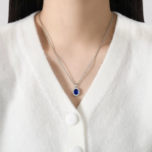 Elegant silver halo necklace with oval blue sapphire pendant worn on a model