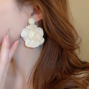 Gros plan de boucles d'oreilles fleurs en tissu crème élégant avec pétales légers