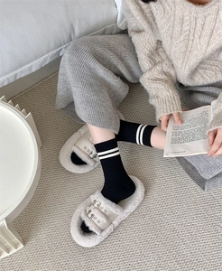 Detail of black mid-tube wool socks with white stripes paired with plush buckle slippers