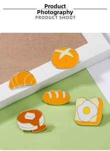 Détail d'un ensemble de 5 broches émaillées en forme de pain et d'œuf sur un fond clair