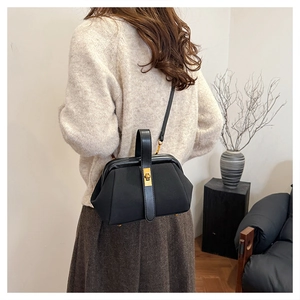 Fashionable black shell bag with vintage metal clasp worn by a model in a cozy setting