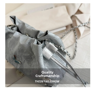 Macro detail of silver pleated fabric bag featuring a blue butterfly metal ornament