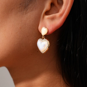 Close-up of heart-shaped earring with cream cat eye stone and rhinestone border