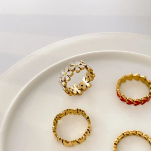 Detail of four gold rings with daisy and heart charms on a white ceramic plate