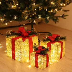 Close-up of golden LED Christmas gift boxes with red ribbons and festive pine needles