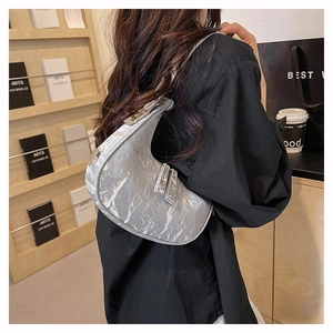 Detailed view of a silver crescent underarm bag with pleated metallic texture on a model