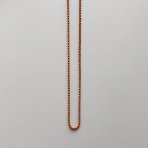 Nahaufnahme einer leuchtend orangefarbenen Kette vor einem schlichten cremefarbenen Hintergrund