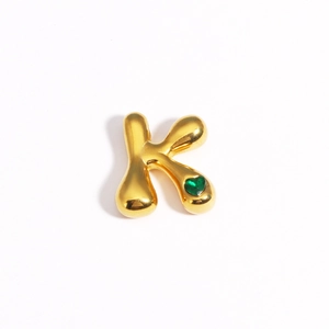 Vue détaillée du pendentif lettre K dorée avec une pierre précieuse verte en cœur