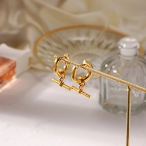 Detailed view of golden geometric T-bar pendant hoop earrings on white silk