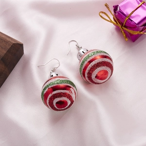 Close-up of red Christmas bulb earrings with glitter stripes on pink satin background